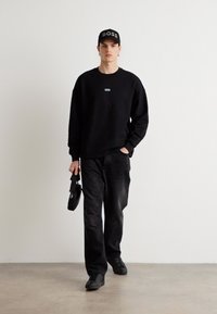 Černá mikina s malým logem na hrudi, doplněná černými kalhotami. Černá čepice s nápisem "BOSS." Černé boty dokončují outfit.