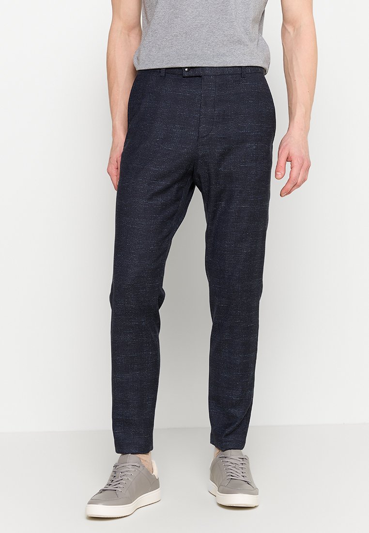 Navy textuurbroek met een slim fit, voorzien van riemlussen en een knoopsluiting. Gecombineerd met grijze sneakers voor een casual uitstraling.