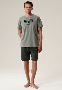 Zielona koszulka z krótkim rękawem z grafiką "WILD MAN", w połączeniu z ciemnozielonymi szortami, wykonana z miękkiego materiału, idealna na co dzień.