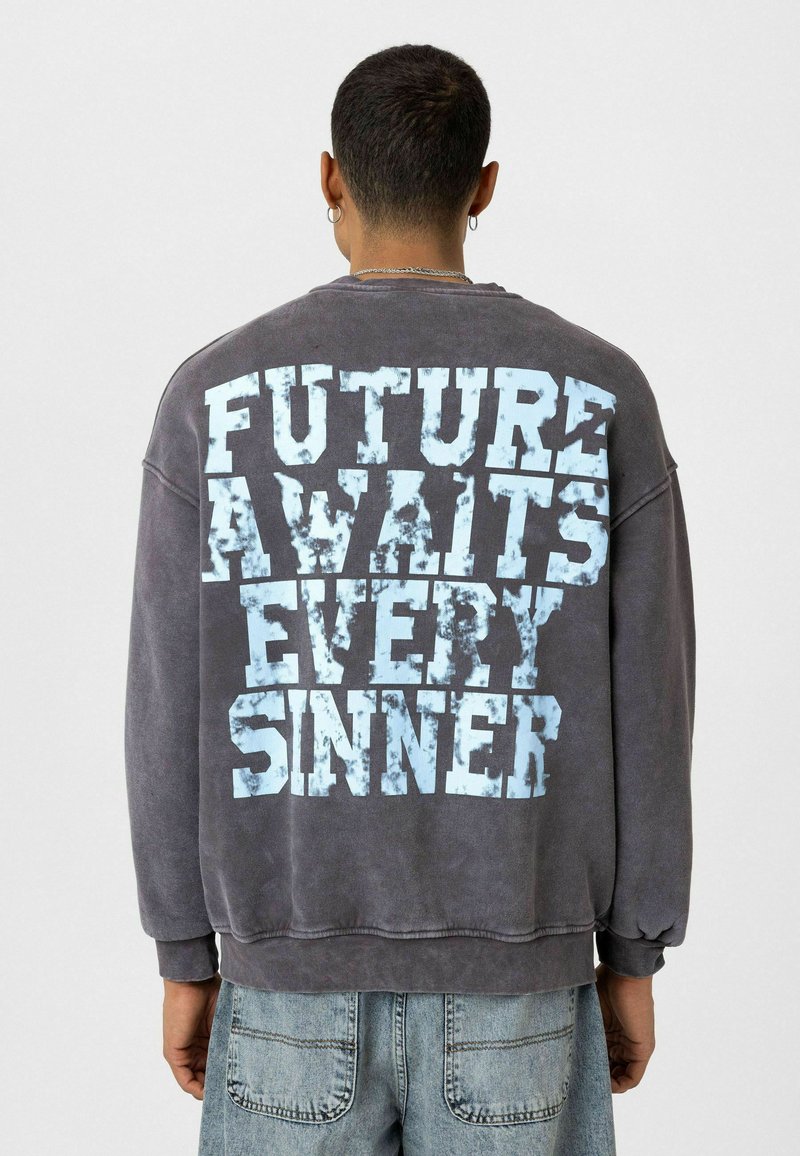 Overgrote grijze sweatshirt met op de rug versleten blauwe tekst: "DE TOEKOMST WACHT OP IEDERE ZONDAR." Lange mouwen en ribgebreide manchetten.