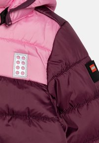 Chaqueta acolchada con parte superior rosa y parte inferior púrpura oscura, con una etiqueta del logo de LEGO y un parche rectangular único con diseños circulares.