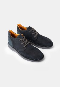 Pantofi din suede albastru închis, cu șireturi gri, căptușeală interioară bej, vârf rotund și cusături contrastante pe o talpă din cauciuc.
