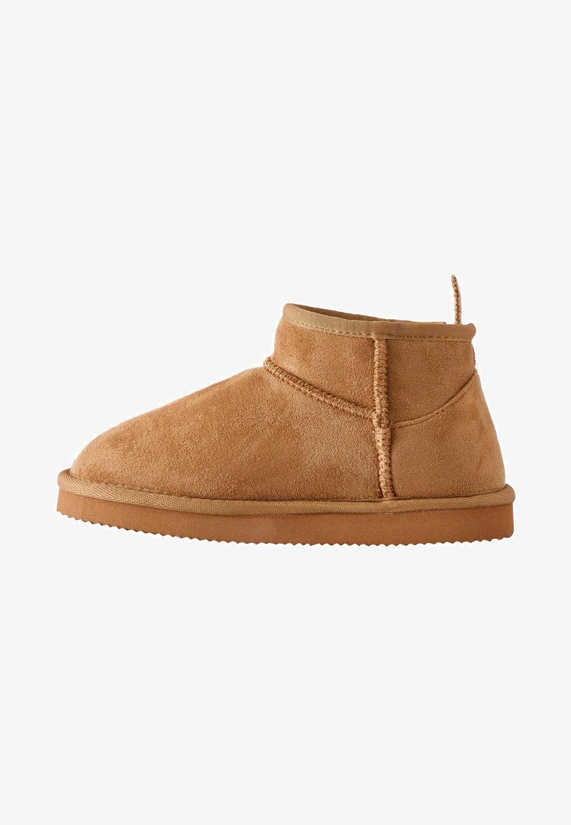 Bottines en suede beige avec un bout arrondi, un détail élastique sur les côtés et une semelle en caoutchouc texturée. Comprend une boucle à l'arrière pour un enfilage facile.