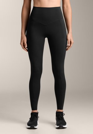 Leggings neri a vita alta con una fascia in vita a forma di V, texture liscia e pannelli laterali a contrasto. Presentano una silhouette aderente.