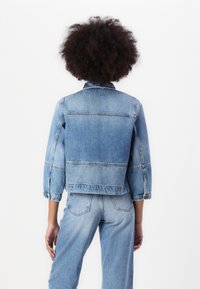 Denim jacket in light blue, cropped design with a classic collar, buttoned cuffs, and visible seam details on the back and shoulders.