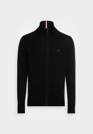 Black zip-up sweater with a high collar, featuring a red and white stripe at the neck and small logo on the chest. Soft fabric and fitted design.