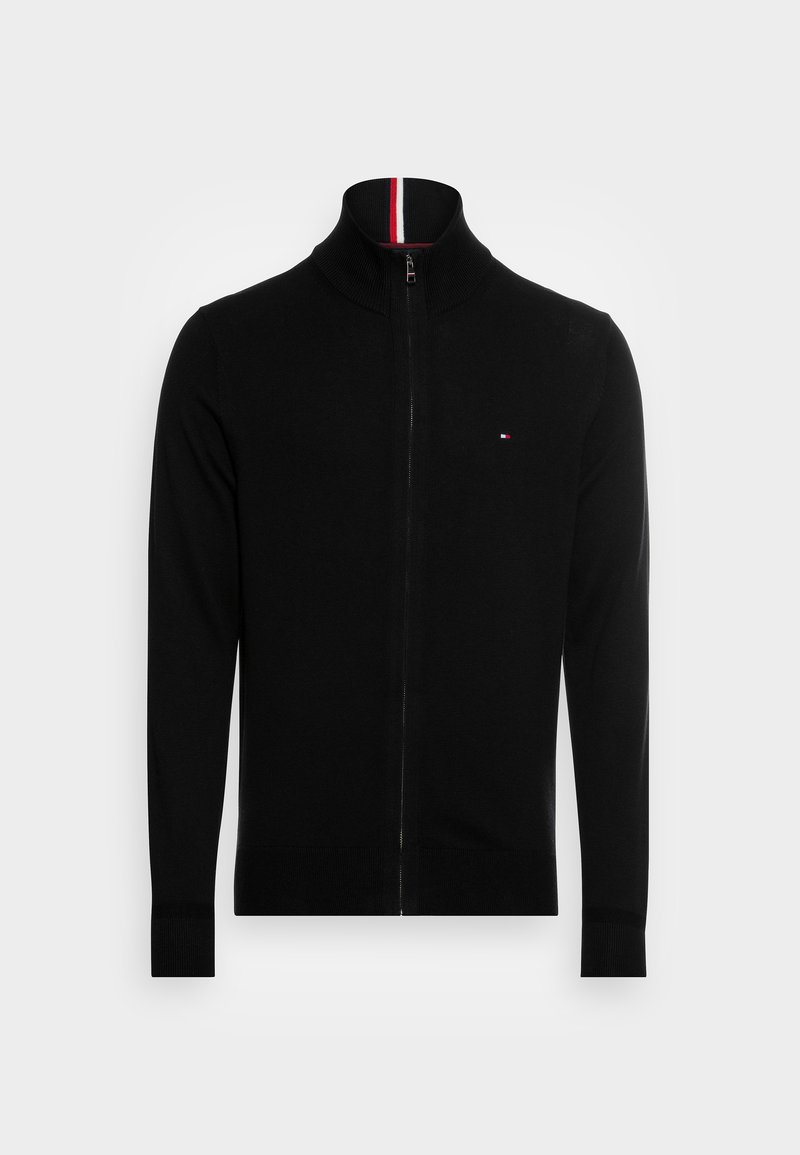 Pull à zip noir avec un col montant, doté d'une bande rouge et blanche au niveau du cou et d'un petit logo sur la poitrine. Tissu doux et design cintré.