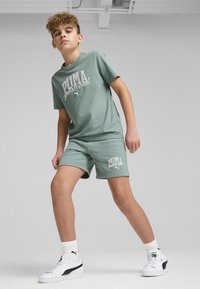 Conjunto de camiseta de algodón verde claro y pantalones cortos con el logotipo blanco "PUMA sports club". Equipado con zapatillas blancas con acentos negros y calcetines de canalé.