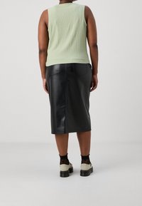 Jasnozielony, teksturowany top bez rękawów zestawiony z czarną skórzaną spódnicą midi. Czarne buty z białymi podeszwami i przezroczyste skarpetki w kropki dopełniają całość.