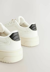 Witte sneakers met een gladlederen bovenwerk, zwarte leren accenten op de hak en een gestructureerde rubberen zool. Minimalistisch ontwerp.