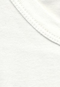 Gros plan sur un tissu blanc montrant la texture tricotée et le détail de la couture d’un bord de col côtelé sur un vêtement en coton uni.
