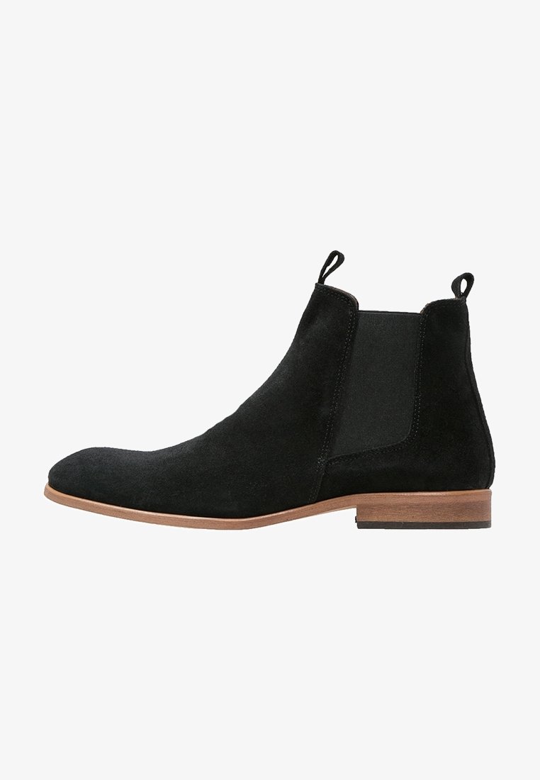 Botte Chelsea en daim noir avec semelle en bois marron, panneaux latéraux élastiques et languettes sur le col de la cheville.