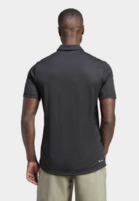 Czarna koszulka polo z krótkim rękawem, uszyta z gładkiego, lekkiego materiału. Posiada kołnierzyk oraz małe logo u dołu, dopasowany krój i minimalistyczny design.