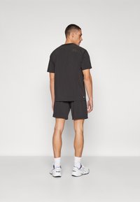 Mørk grå idretts t-skjorte med korte ermer, kombinert med matchende shorts. Brukt med hvite joggesko med blå detaljer.