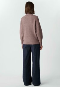 Jasnoszary sweter z dzianiny o prążkowanej fakturze i z kołnierzem kominowym, zestawiony z ciemnoniebieskimi szerokimi spodniami, widziany od tyłu.