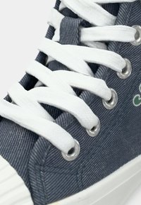 Καμβάς αθλητικό παπούτσι με γκρι ριγέ σχέδιο, λευκά κορδόνια, ασημένιους οφθαλμούς και λευκή καουτσούκ σόλα. Κοντινή όψη του πάνω μέρους.