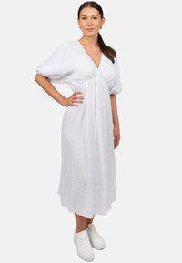 Witte, knielange jurk van gestructureerde stof met een V-hals, korte puffmouwen en een relaxed fit, gecombineerd met witte sneakers.