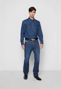 Denim shirt and jeans set in medium blue; shirt features two chest pockets and snap buttons, jeans are straight-cut with a classic fit. Black belt with silver hardware.