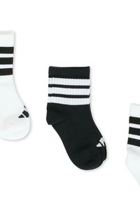 Tres pares de calcetines: uno negro con tres rayas blancas en la parte superior, uno blanco con rayas negras, y uno blanco con dos rayas negras en la punta.