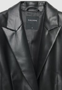 Blazer in pelle nera con colletto a punte, texture liscia e etichetta interna con "CALLIOPE" e taglia "S".