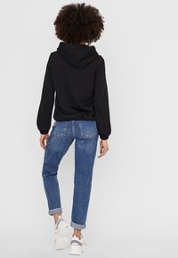 Schwarzer Hoodie mit lockerem Schnitt, gerippten Bündchen, kombiniert mit hellblauen hochgekrempelten Denim-Jeans und weißen Sneakern. Flauschige Ärmelfläche sichtbar.