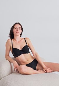 Melna apakšveļa, kas sastāv no krūštura ar mežģīņu maliņām un atbilstošām bikini biksēm. Mīksts, gluds materiāls ar regulējamiem siksniņām.
