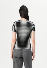 T-shirt de manga curta listrado em preto e branco com um design ajustado e textura ribete. Decote redondo e detalhe do logotipo nas costas.