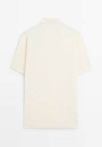 Polo à manches courtes de couleur crème claire, doté d'un col classique et d'une texture douce et lisse, sans motifs ni détails métalliques visibles.