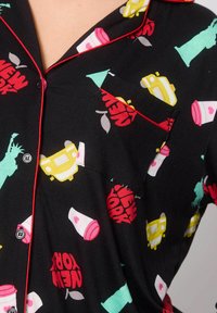 Camisa de pijama negra con gráficos coloridos inspirados en Nueva York, que incluyen taxis, tazas de café y la Estatua de la Libertad. Detalle de ribete rojo.