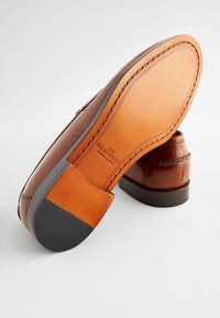 Braunes Leder-Schuhwerk mit glatter Oberfläche und detaillierter Naht. Verfügt über eine kontrastierende sandfarbene Sohle mit einer schwarzen Gummikappe.