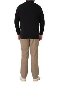 Schwarzer Strickpullover mit Kragen, kombiniert mit beigen Hosen und weißen Schuhen. Der Pullover hat eine glatte Struktur und gerippte Bündchen.