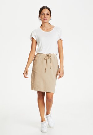 Lightweight white t-shirt paired with a beige skirt featuring a drawstring waist. Model wears white sneakers, standing against a plain background.