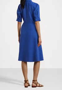 Blå linnklänning med korta uppvikta ärmar, A-linjeformad silhuett och knälång nederkant. Ett par bruna sandaletter med remmar fulländar looken.