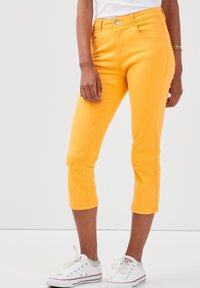Gele cropped denim broek met een aansluitende pasvorm, vijf zakken en stiksels, gecombineerd met witte sneakers.