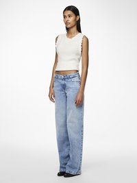 White ribbed knit sleeveless top with scalloped trim, paired with light blue wide-leg jeans. Black pointed-toe shoes, neutral background.