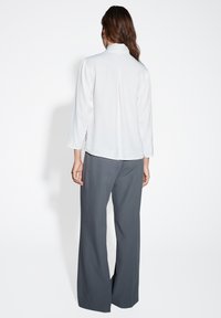 Maglietta bianca con colletto alto e maniche lunghe, abbinata a pantaloni larghi grigi. Tessuto morbido e silhouette rilassata.