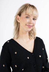Cardigan nero con scollo a V, caratterizzato da motivi a cuore dorati e bottoni neri lungo il davanti. Texture morbida, design casual, stile versatile.