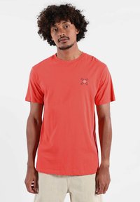 T-shirt corail à manches courtes en tissu doux, avec un petit motif imprimé sur le côté gauche de la poitrine, col rond et coupe décontractée.