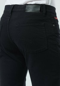 Jean en denim noir avec étiquette en cuir sur la taille, deux poches arrière avec des détails de couture et une coupe slim.