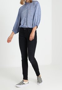 Camisa de botones azul claro con patrón floral, jeans ajustados negros y zapatillas slip-on de cuadros en blanco y negro.