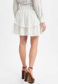 Weißer Rock mit floralem Druck und zwei Schichten Rüschen, mit gefälteltem Taillenbund und gewelltem Saum, kombiniert mit braunen High-Heel-Sandalen.