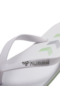 Vit flip-flop med en texturerad sula, med en vit rem, gröna och grå geometriska accenter samt en silverfärgad "hummel"-logotyp.