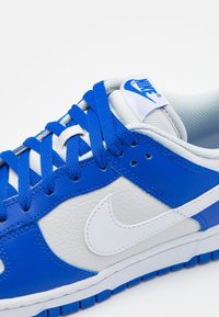 Nike sneakers featuring a blue and white leather upper, textured panels, flat blue laces, and a white swoosh logo on the side.