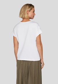 White cotton T-shirt with short sleeves and a relaxed fit, featuring a rounded neckline and slight drop tail hem, paired with a pleated olive skirt.