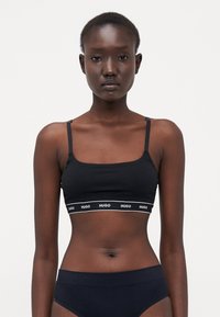 Black bra with thin straps, featuring a branded elastic band at the bottom. Simple, fitted design with a smooth texture.
