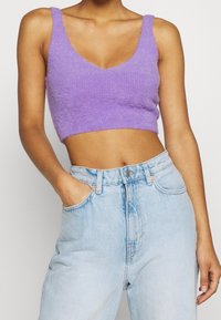 Top corto morado con escote en V, textura esponjosa y tirantes anchos, combinado con jeans de mezclilla de corte alto en azul claro con bolsillos laterales.