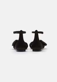 Ballerine in suede nero con cinturini alla caviglia, design a punta tonda e dettaglio a fiocco decorativo sulla parte anteriore. Texture liscia, stile sobrio.