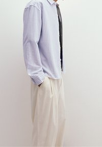 Chemise rayée violet clair avec des lignes bleues, manches longues, une seule poche, associée à un pantalon large de couleur crème. Texture de tissu lisse.