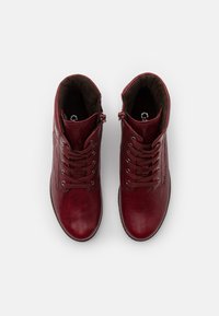 Botas de tobillo de cuero burdeos con superficie texturizada, punta redonda, diseño con cordones y cremallera lateral para facilitar el uso. Interior forrado con material suave.