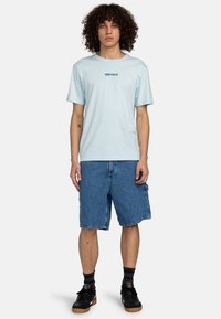 Lyseblå bomulds t-shirt med "element" logo i mørkegrøn, parret med denim cargo shorts og sorte sneakers. Enkel design, afslappet pasform.